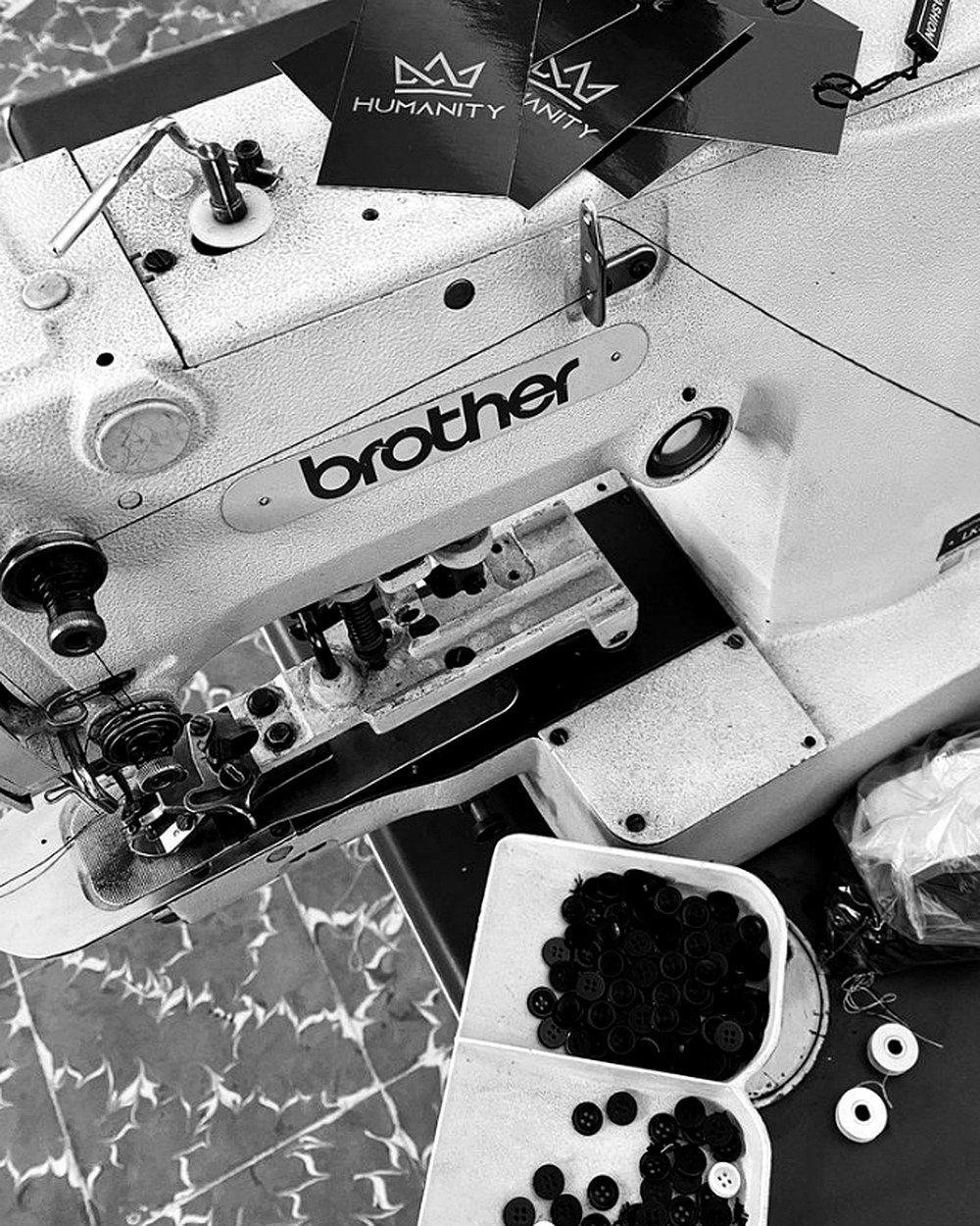 Máquina de coser industrial en el taller de Humanity, con hangtags de la marca y bobinas de hilo